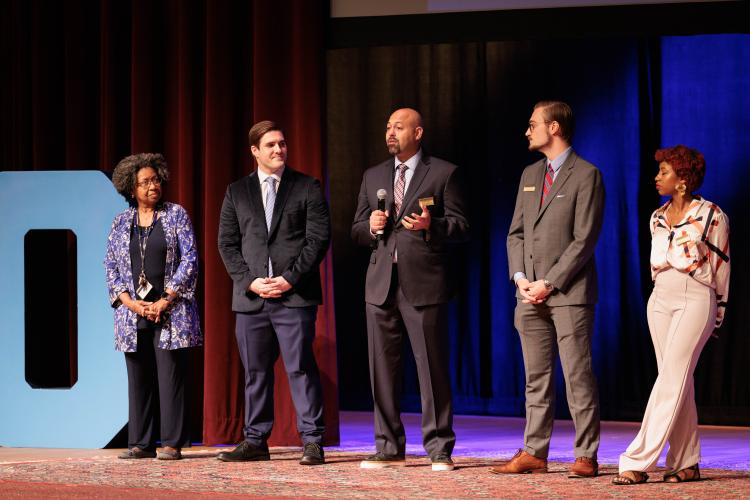 A group of people standing in a line on stage with a microphone