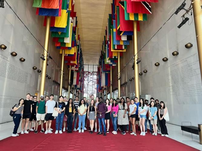 Students standing in a large hall with flags of the world