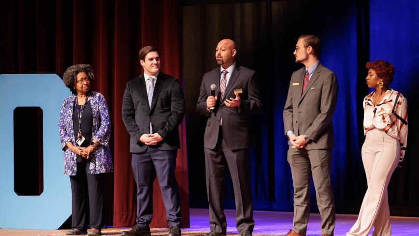 A group of people standing in a line on stage with a microphone