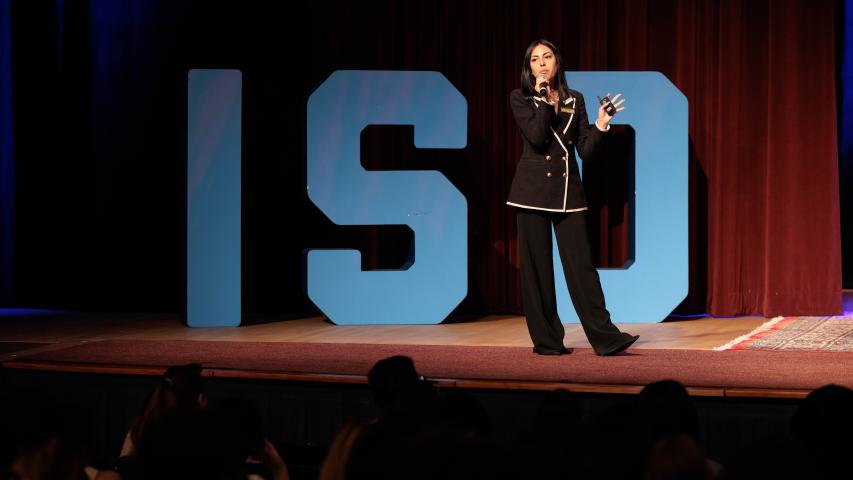 A presenter on stage in front of large letters that read ISO
